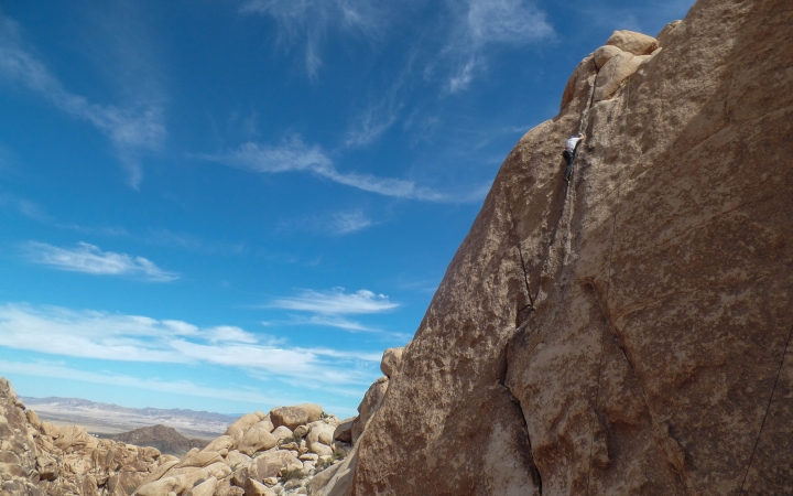 A rock climber is near the top of a rock wall with blue skies above